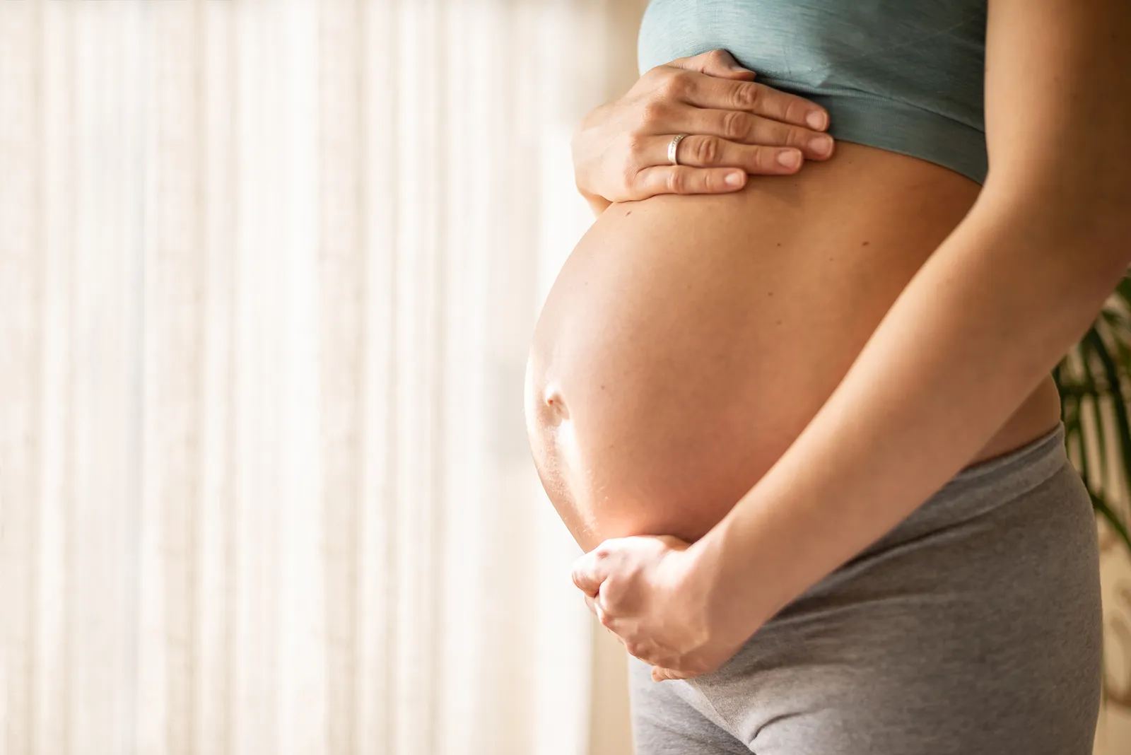 Womans bare pregnant belly being cradled by her arms